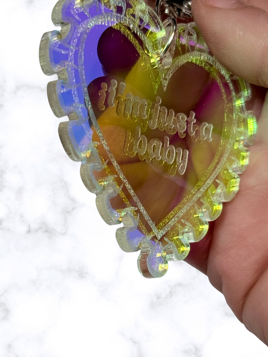 Iridescent heart acrylic keychain with "Just a Baby" inscription by Adorrible, featuring a shiny, reflective surface and a metal keyring.