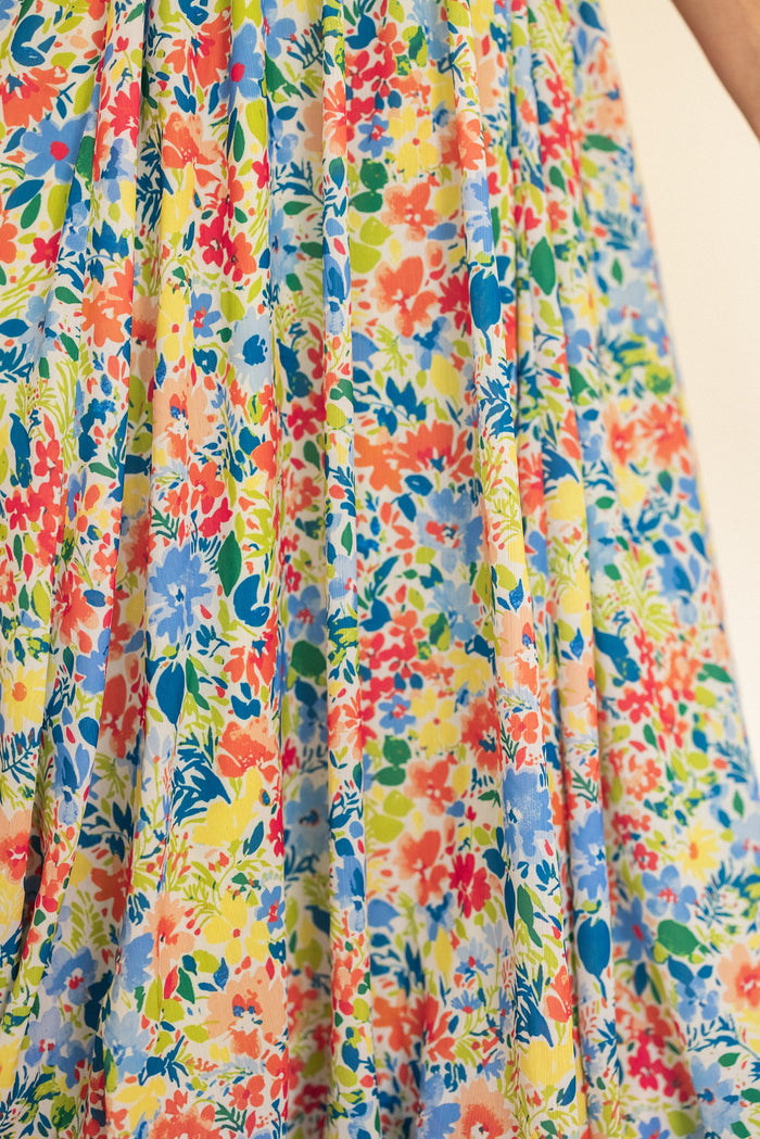 A close-up of the Ada Dress in Vibrant Yarrow Print by Ivy City Co, a flowing floral chiffon dress with red, orange, yellow, blue, and green flowers on a light background—perfect for a maternity-friendly wardrobe.