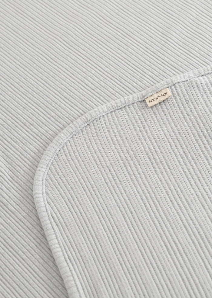 Lysegråt ribstrikket tæppe med buet kant og mærke på folden

Light gray ribbed blanket with curved edge and label on the fold