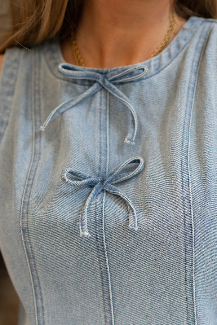 Close-up of a person wearing the Austin Dress in Light Wash Denim by Ivy City Co, featuring two small front bows and a gold chain necklace. The stretch fabric ensures comfort, with the focus on the upper chest area.