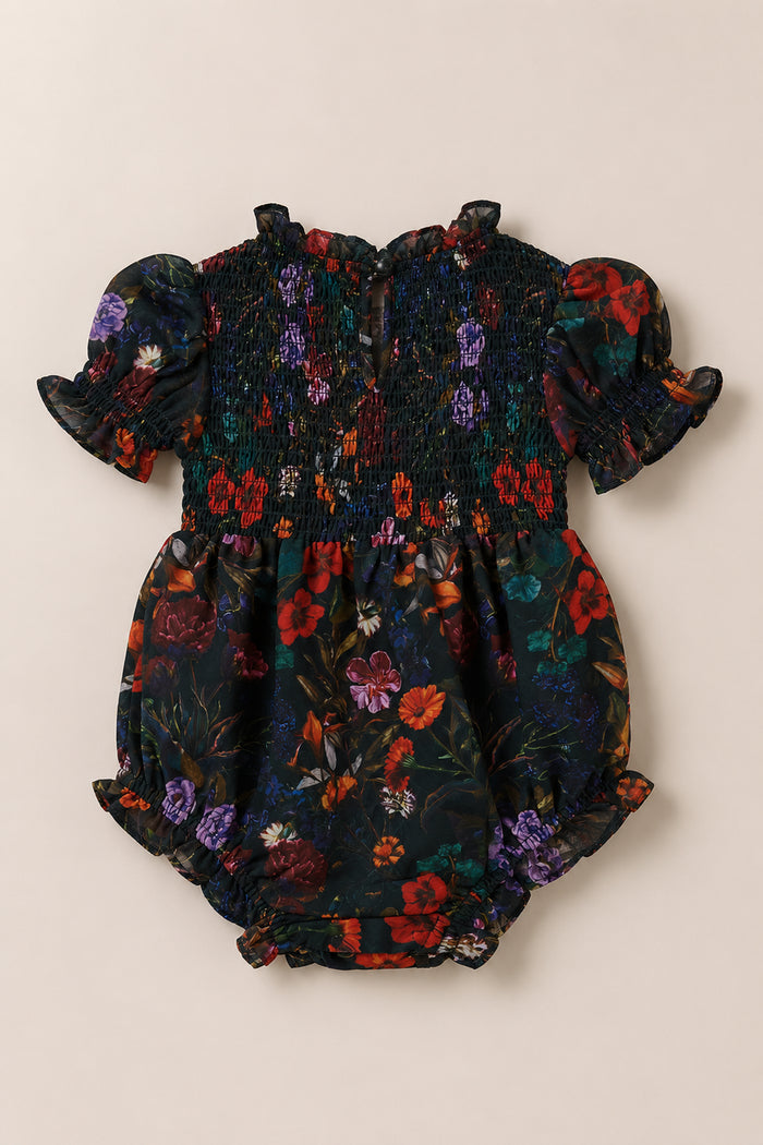 Dress your little one in the Ivy City Co Baby Cordelia Romper in Evergreen Vivid Meadow, featuring short puffed sleeves, a smocked bodice, and a dark floral print with red, purple, and orange flowers and green leaves on a black background—perfect for a charming fall baby outfit.