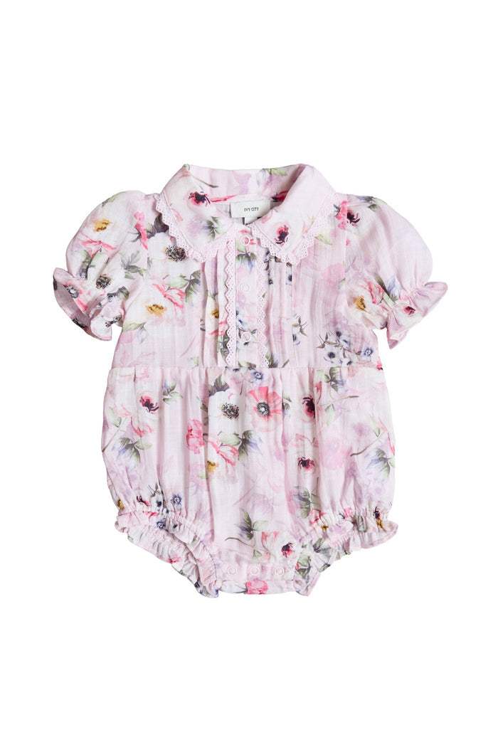The Ivy City Co Baby Sophia Romper in Roselyn Pink features a floral print, short puffed sleeves, scalloped collar, lace chest detailing, and gathered elastic at sleeves and legs—a charming choice for mommy-and-me outfits.