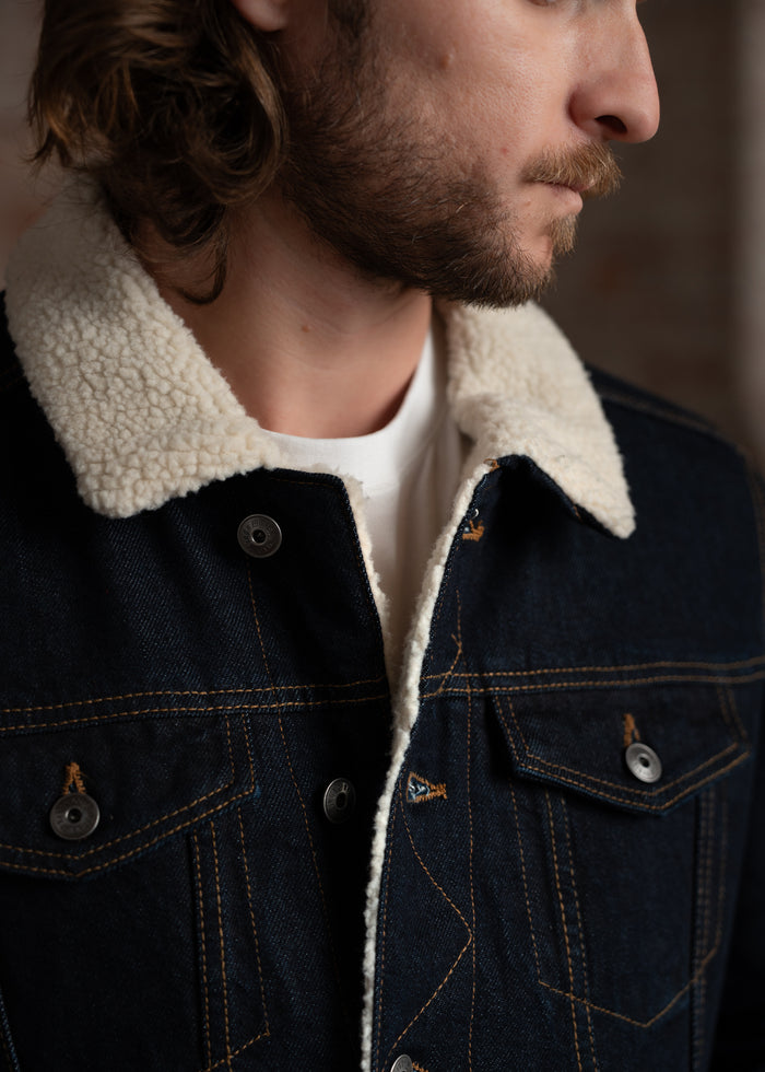 Man in a denim jacket with a shearling collar, side profile, showcasing detailed stitching and button design.