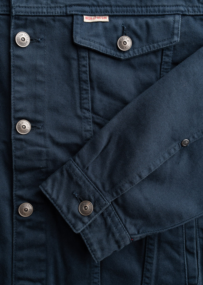 Men’s bull denim trucker jacket in Navy, with button front, welt hand pockets, close-up shot to showcase details of fabric and custom buttons