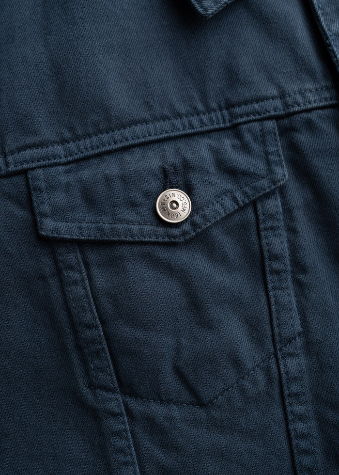 Men’s bull denim trucker jacket in Navy, with button front, chest pockets, close-up shot to showcase details of fabric and custom buttons