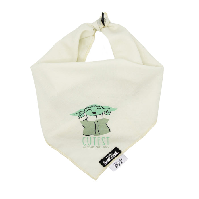 The Sassy Woof Dog Bandana - STAR WARS™ The Child™ features a cream color, cartoon Baby Yoda with “CUTEST IN THE GALAXY,” a knotted top, and two tags. Pair it with a matching leash or lightweight cotton collar for extra style.