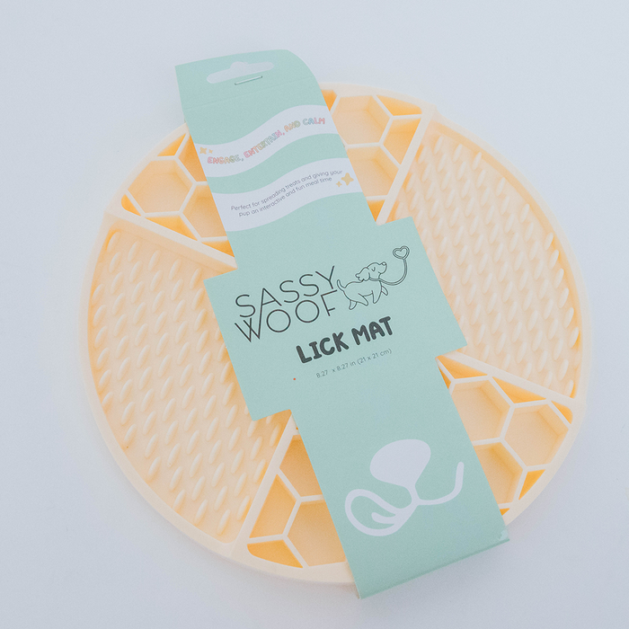 The Sassy Woof Dog Lick Mat is a round, beige silicone mat with a honeycomb pattern for dog anxiety relief, packaged with a mint green label showing a dog illustration and product details.