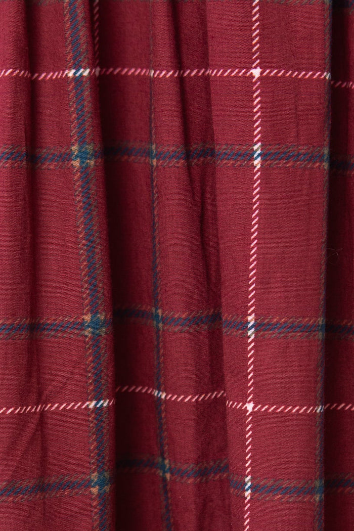 A close-up of the Hattie Dress in Burgundy Plaid by Ivy City Co highlights its white, blue, and black plaid fabric and gathered seam detail—perfect for a stylish midi-length look.