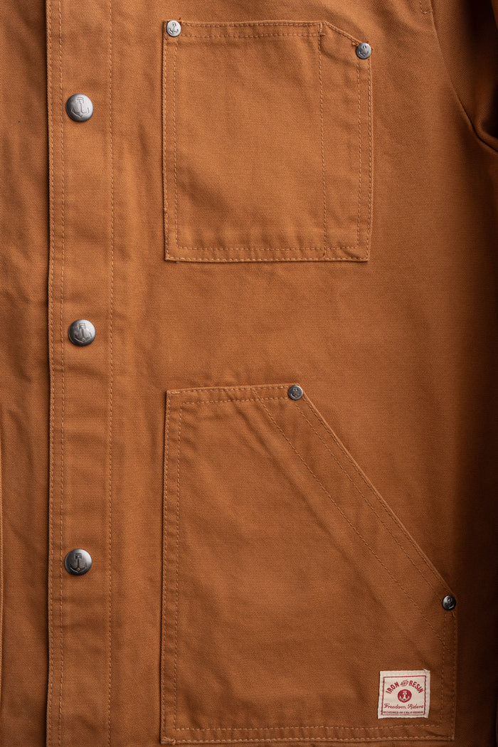 Brown canvas jacket with metal buttons, two front pockets, and a small label at the bottom right corner.