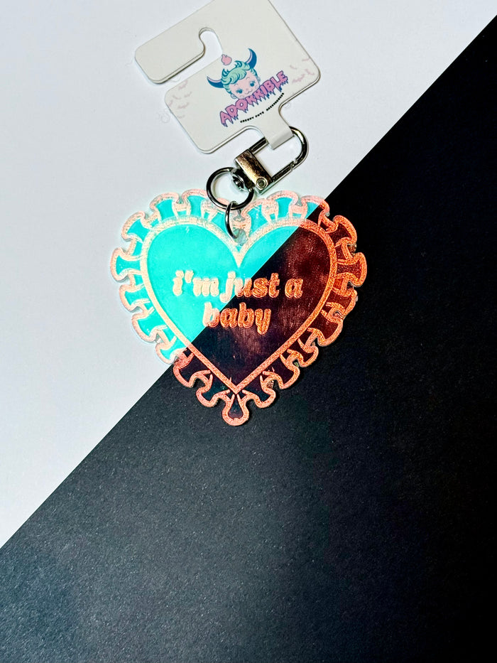 Iridescent heart acrylic keychain with "Just a Baby" text by Adorrible, featuring a shiny, colorful reflective surface.