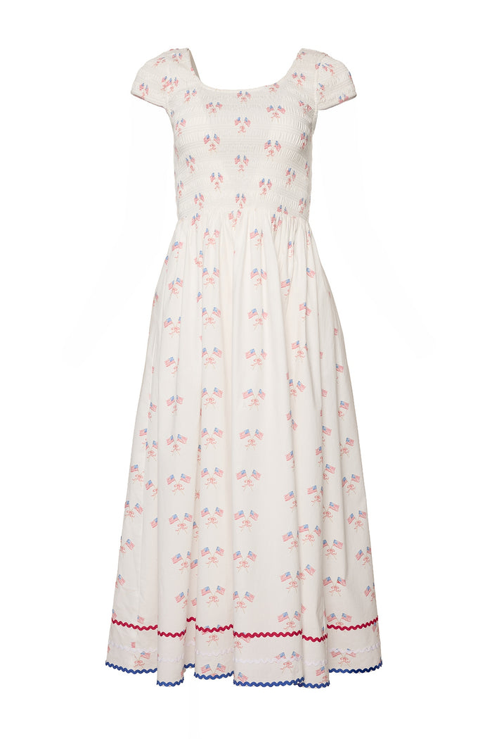 The Marlow Cap Sleeve Dress in Star Spangled by Ivy City Co is a white, ankle-length, maternity-friendly Fourth of July dress with a smocked bodice, cap sleeves, small American flags, and red and blue rickrack trim.