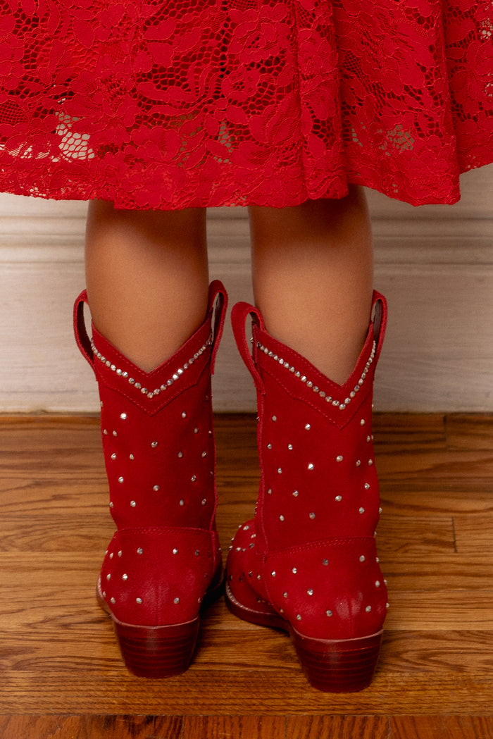 A child in a red lace dress and Ivy City Co's Mini Channing Bootie in Red stands on a wooden floor, facing away—perfect for a mommy-and-me twinning moment.