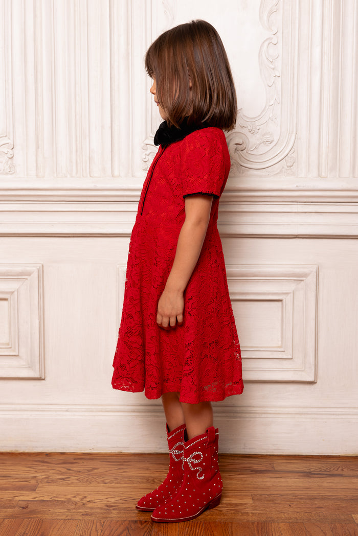 Child wearing a red dress and matching red boots against a white wall.