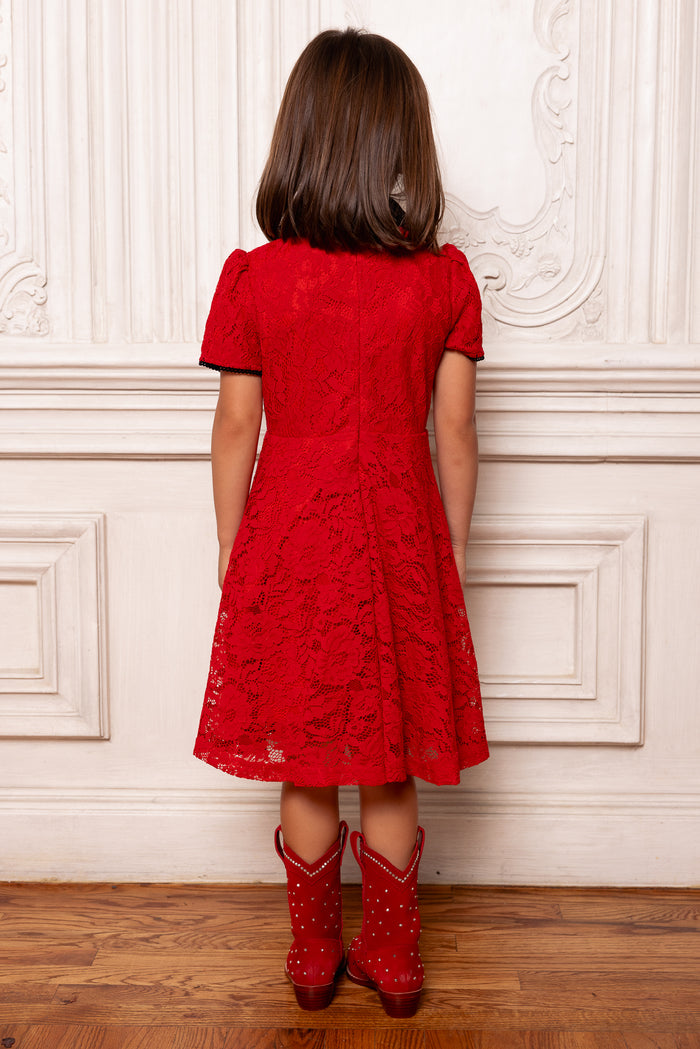 Person wearing a red lace dress and matching red boots against a white wall.