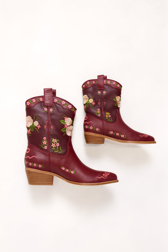 Pair of burgundy cowboy boots with floral embroidery on a white background