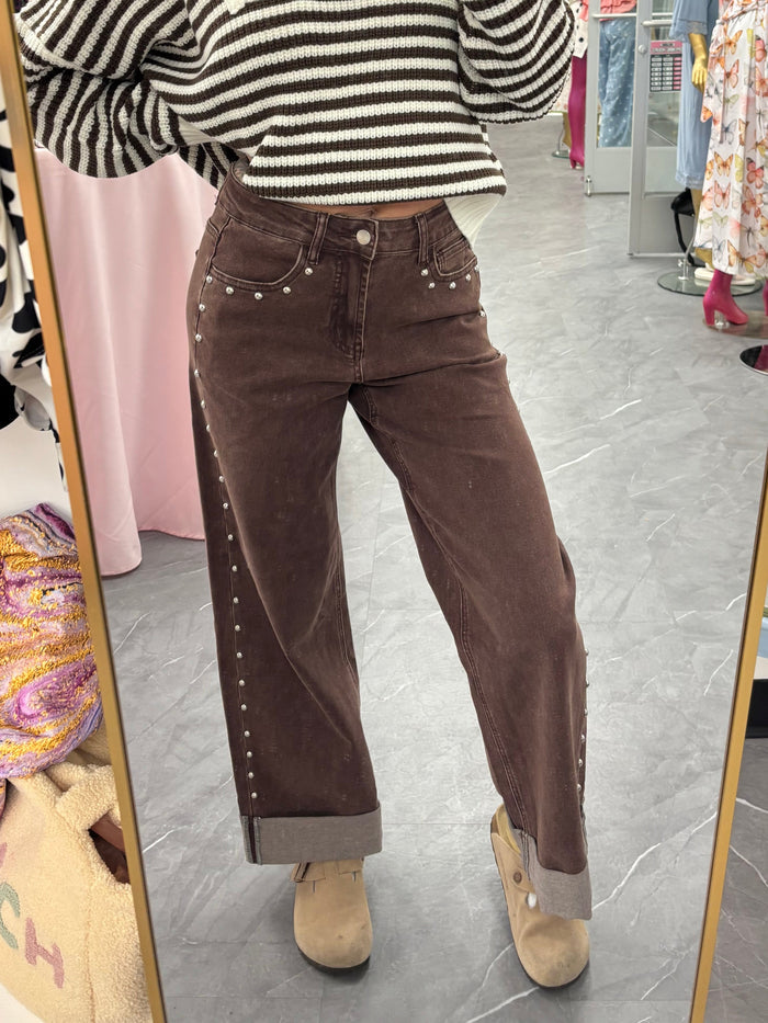 A woman takes a mirror selfie in a clothing store, wearing a black and white striped knit half-zip sweater and brown corduroy pants with silver studs.