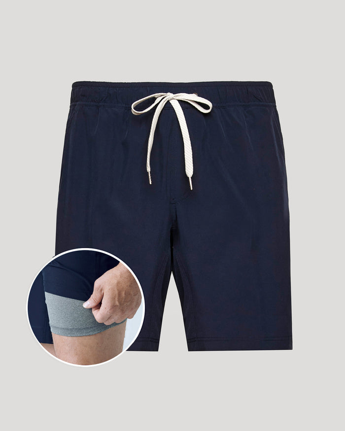 Navy blue shorts with a drawstring on a light gray background, with a close-up inset showing a hand wearing a gray sock.