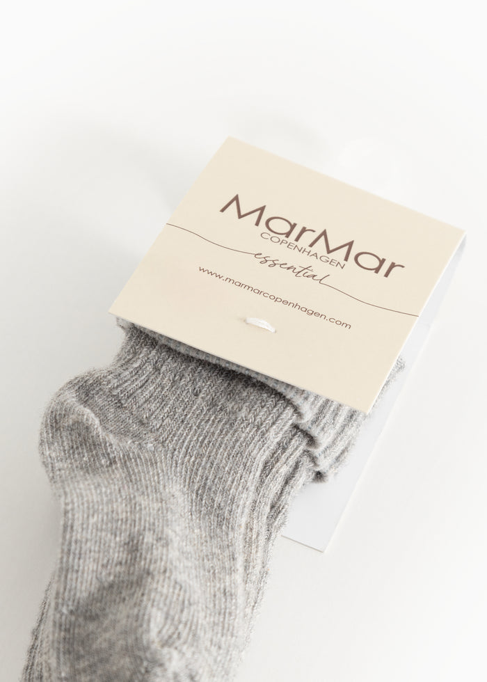 Baby sock in light gray mélange with ribbed edge and short cuff, fastened with a label tag.