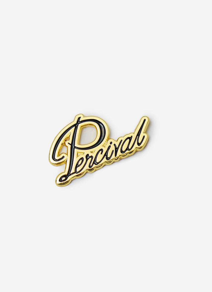 A close-up of the metal Percival Script Pin Badge in a gold finish with black script lettering, against a white background.