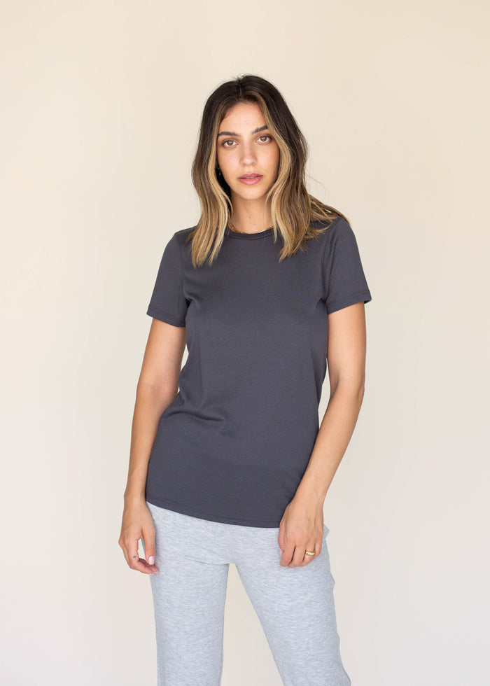 Woman wearing a dark gray t-shirt and light gray pants against a beige background