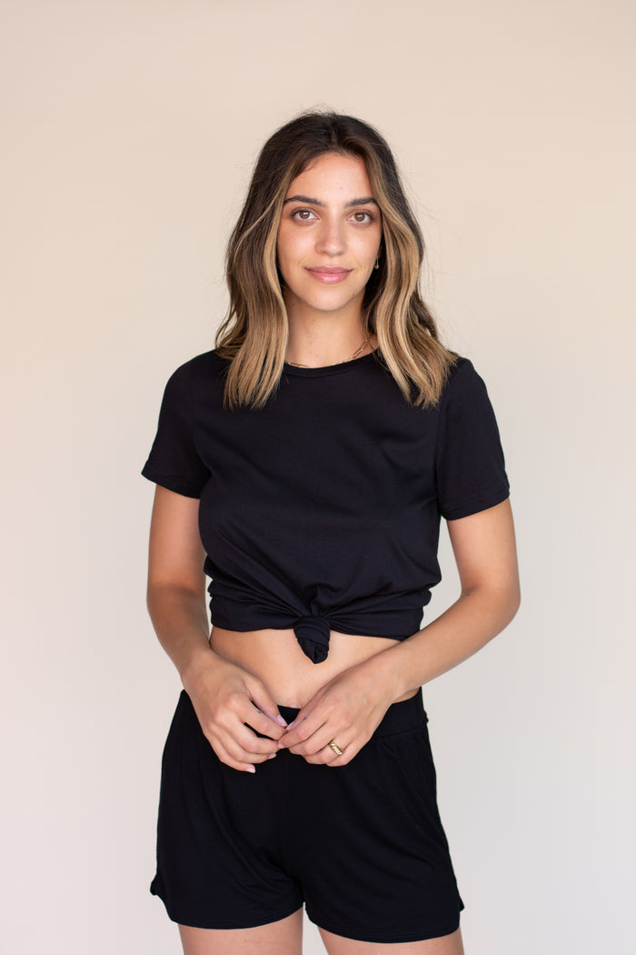 Woman wearing black tee shirt tied into a knot in the front, with black shorts.