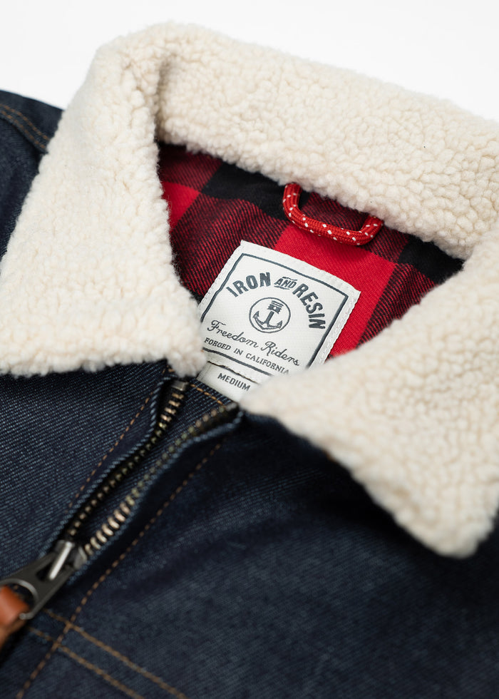 Denim jacket with a sherpa collar, red plaid lining, and Iron and Resin label, showcasing rugged style and craftsmanship.