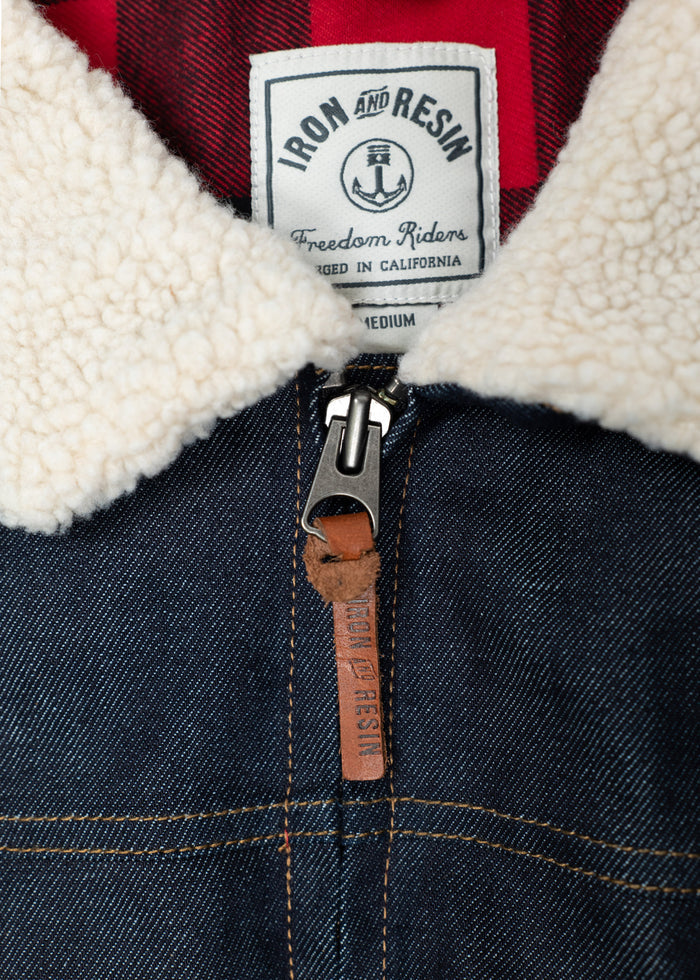 Denim jacket with a sherpa collar, red plaid lining, and "Iron and Resin" label. Features a leather zipper pull.