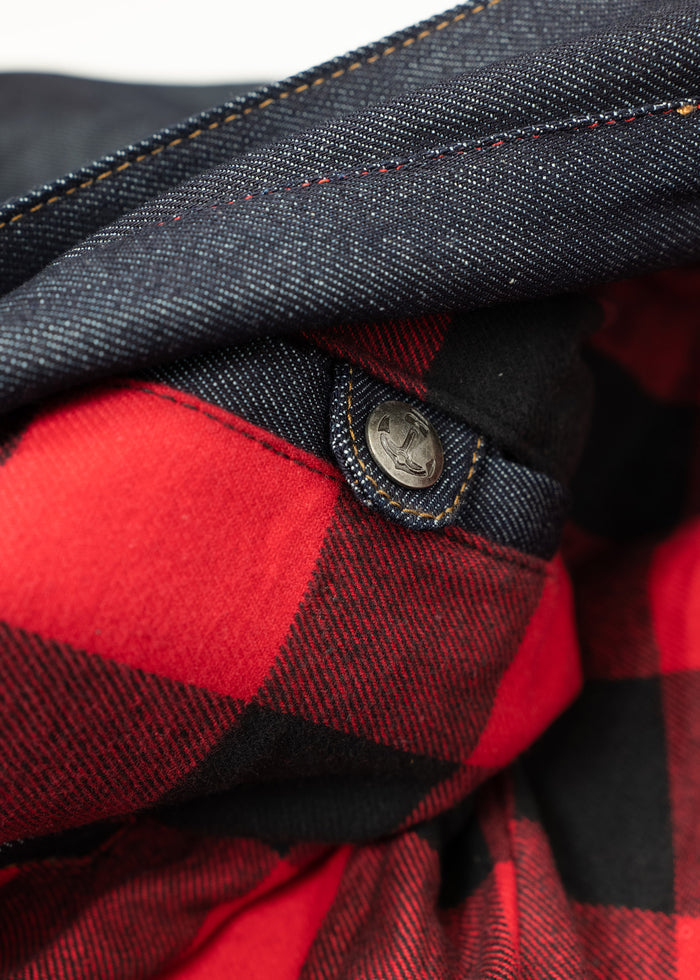 Close-up of a denim jacket with red plaid lining and a metal anchor button, highlighting the contrast in textures and colors.