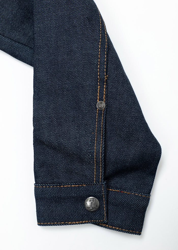 Close-up of a denim jacket sleeve with orange stitching and metal buttons on a white background.