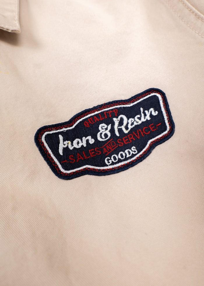 Close-up of a beige shirt with an embroidered "Iron & Resin" patch, featuring "Quality Sales and Service Goods" in red and white.
