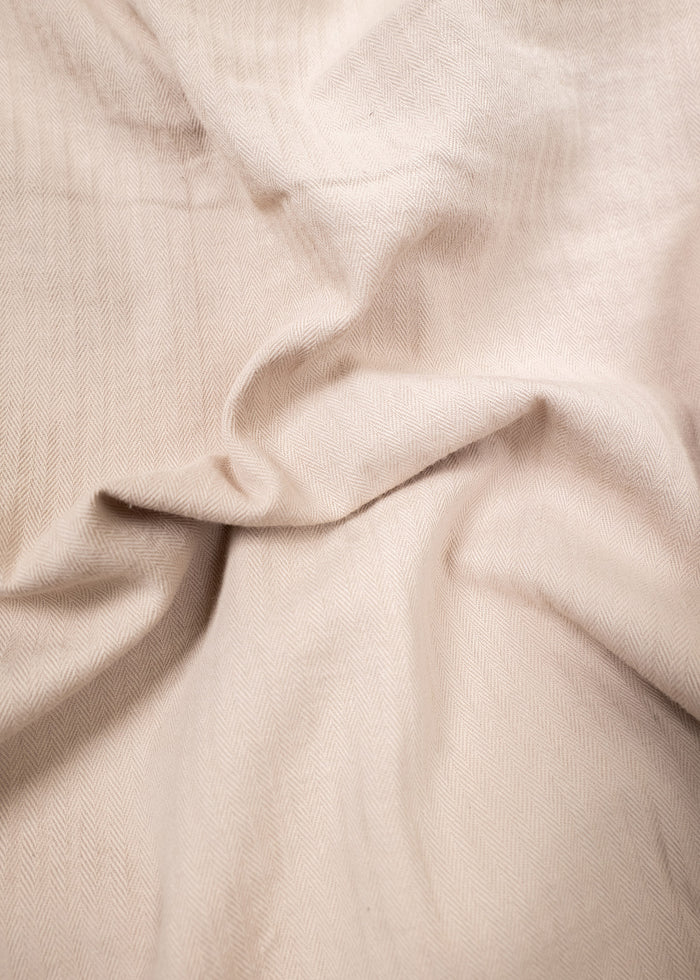 Cream herringbone fabric with soft folds, creating a textured, elegant pattern. The light enhances its subtle, intricate design.