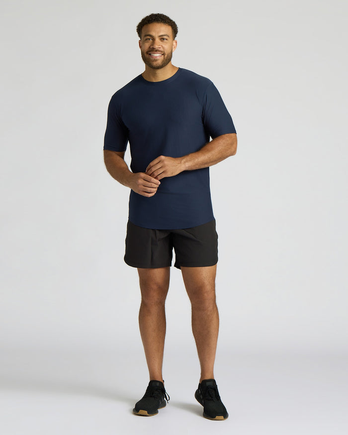 Man wearing a navy t-shirt and black shorts on a light gray background