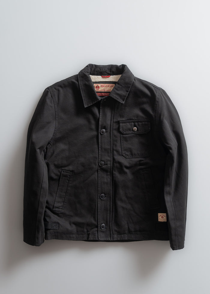 Black jacket with button closure, chest pocket, and branded label on collar. Simple design on a light gray background.