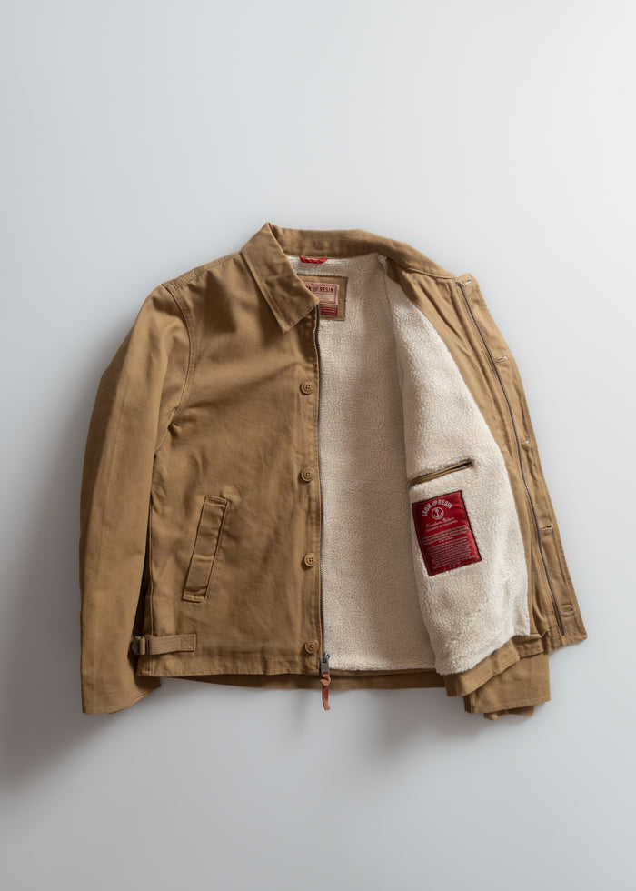 Brown jacket with a cozy white fleece lining, open to reveal a red label inside. Simple design with button closure and pockets.