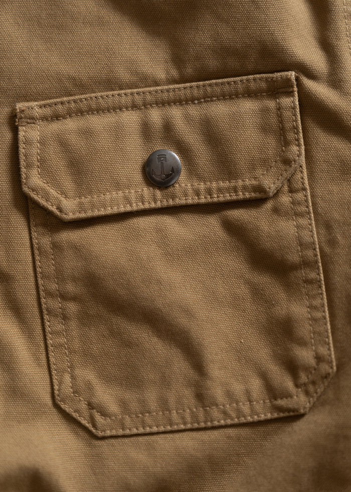 Close-up of a brown fabric pocket with a flap and metal button, featuring an anchor design, on a garment.