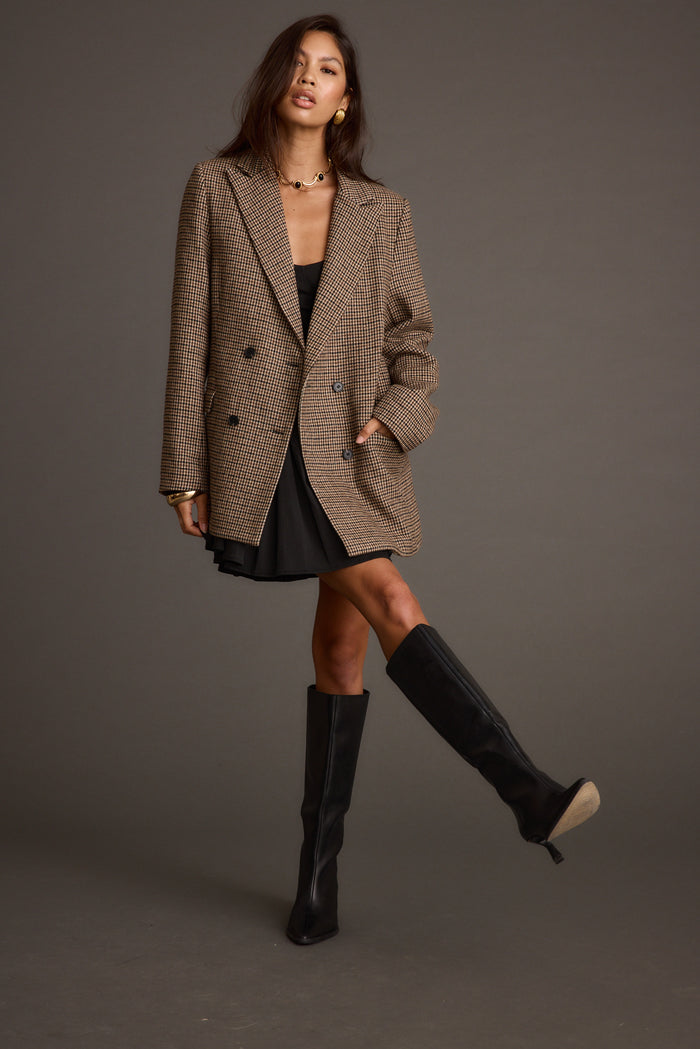 Brown houndstooth plaid blazer styled over a black mini dress with knee-high boots.