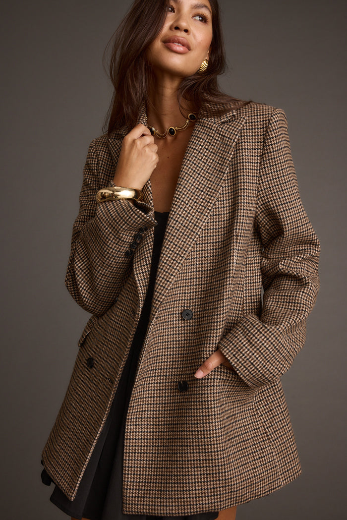 Brown houndstooth plaid blazer worn open over a black mini dress with gold jewelry.